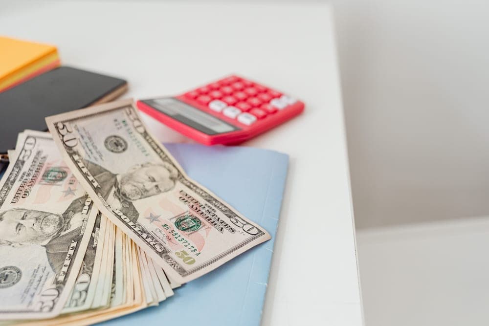 A calculator and a notebook on a desk beside banknotes