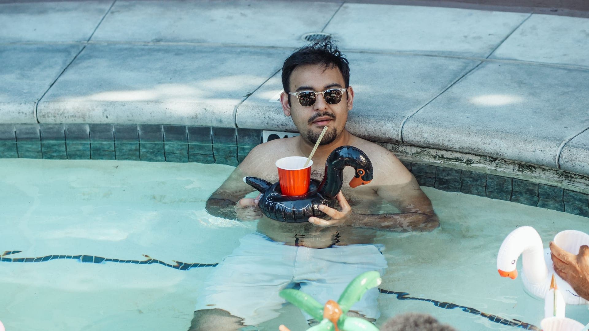 A man in a pool holding a drink beside a float