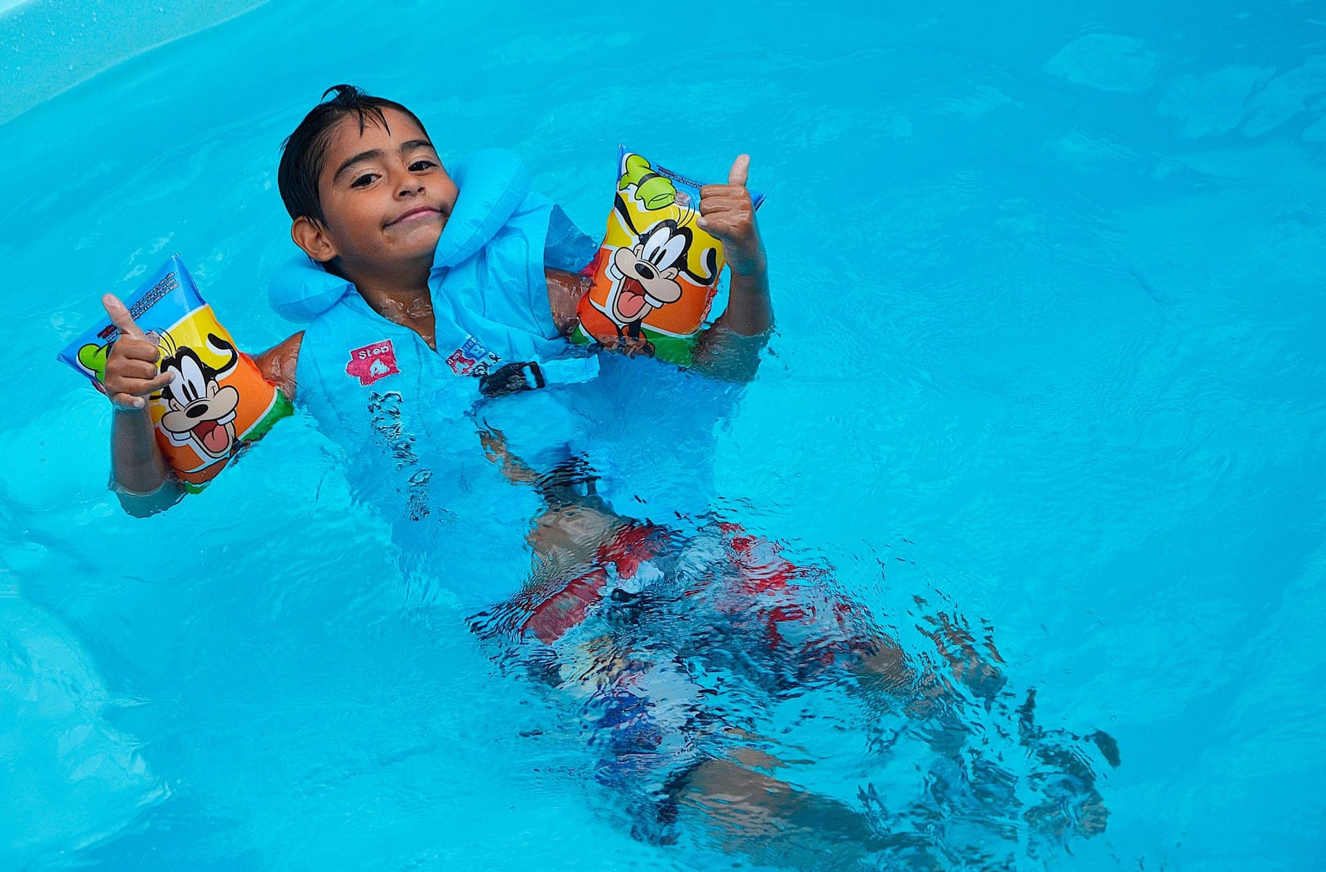 A child in a swimming pool wearing bright armbands