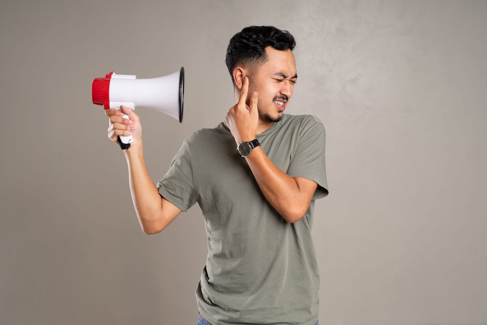 A person covering one ear while holding a megaphone