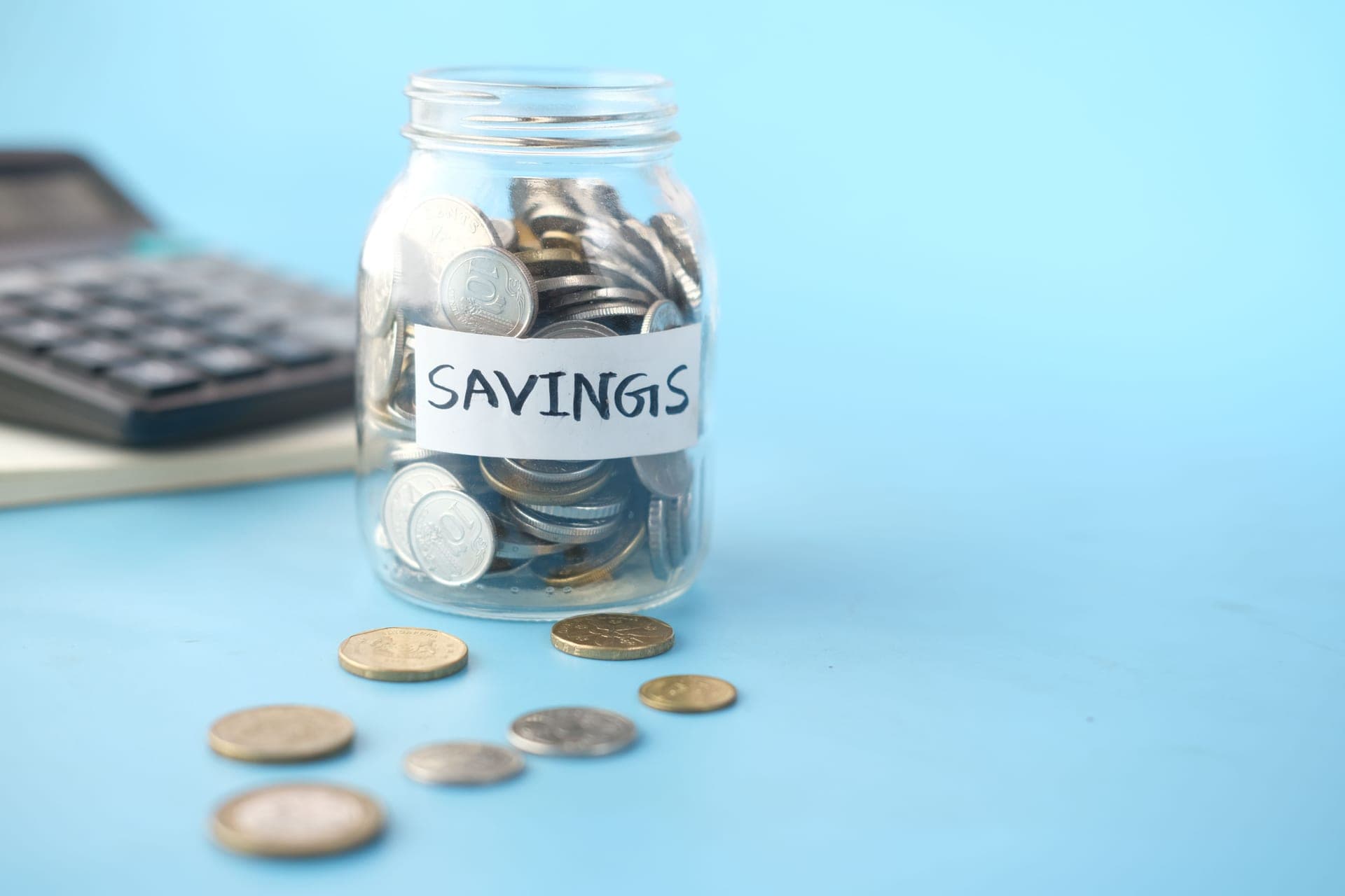 A jar of coins labeled savings beside a calculator