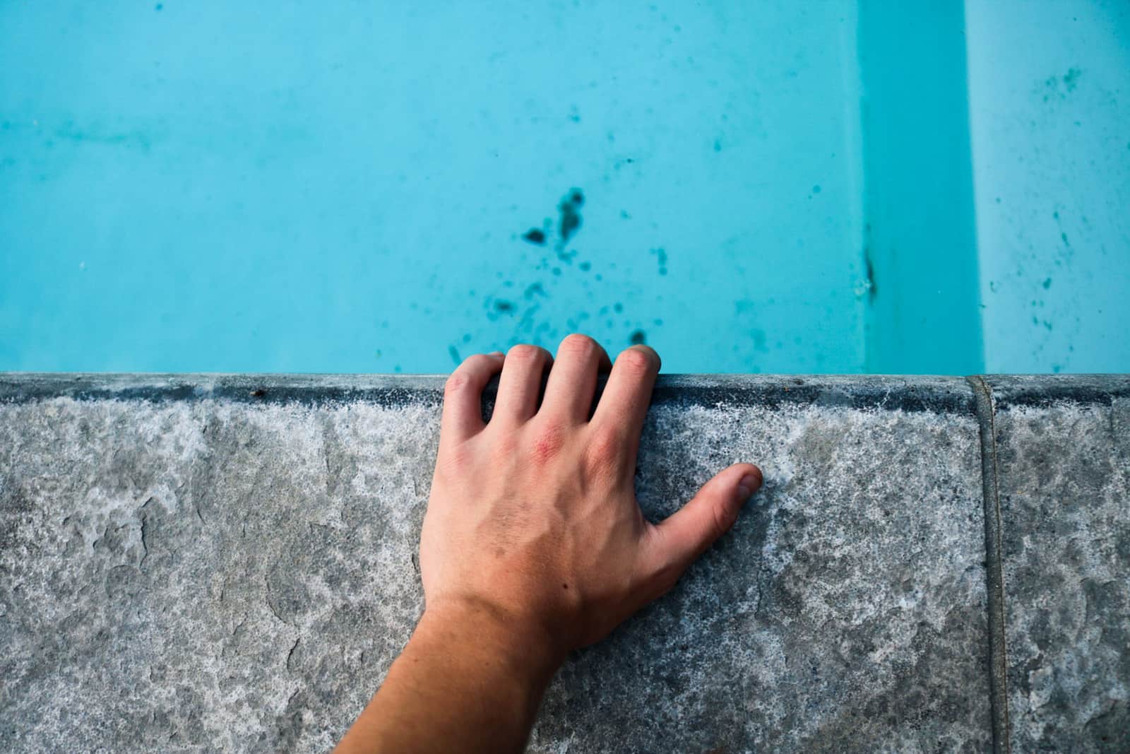 A person skimming leaves from a swimming pool with a net
