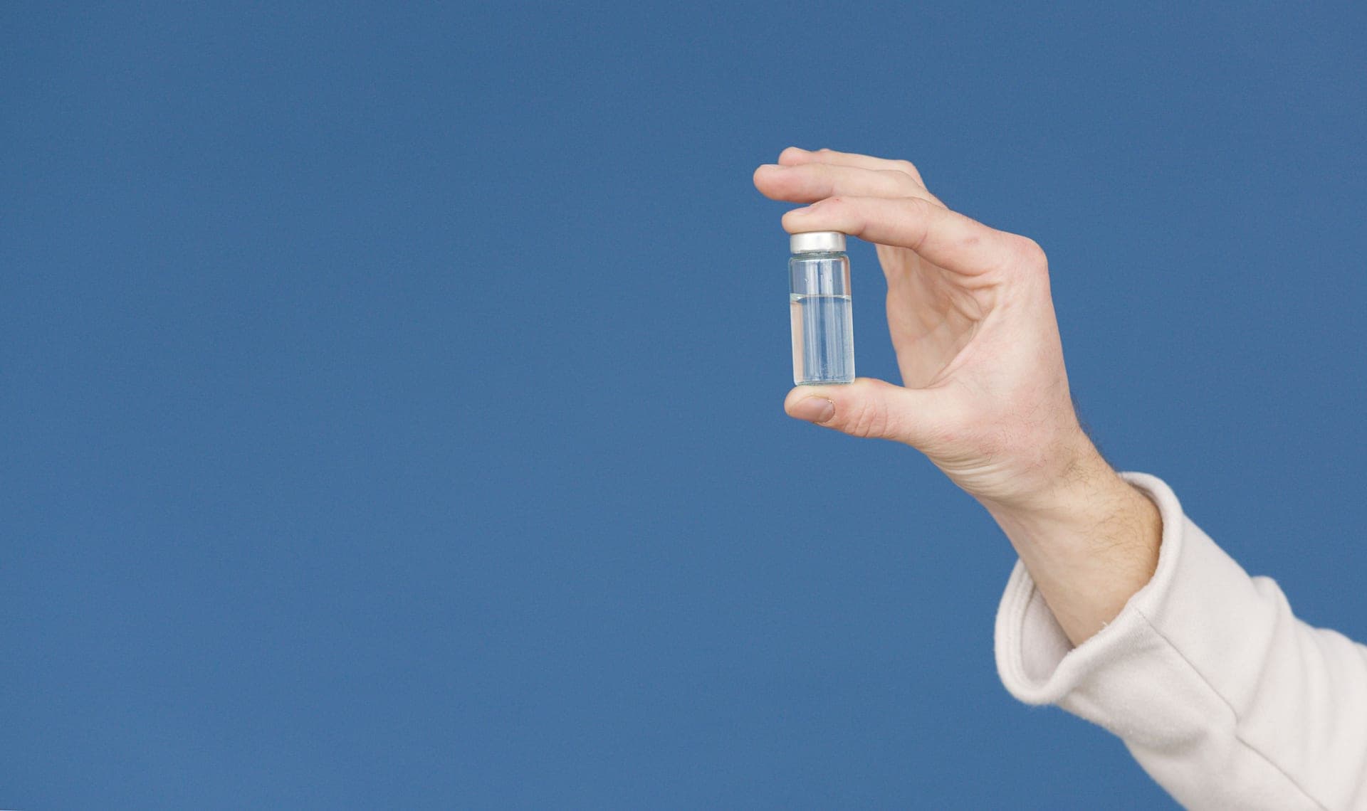 A hand holding a glass test vial of liquid against a blue background